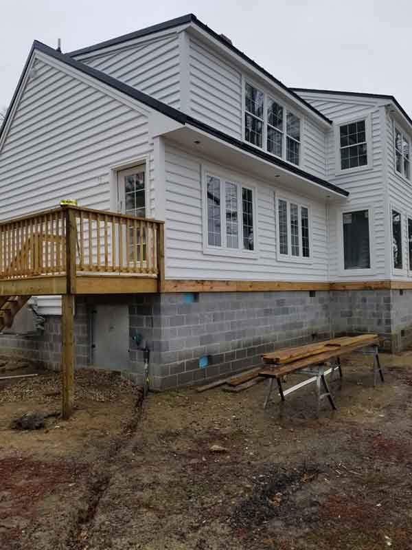 The finished exterior complete with new white siding and a side porch with a new wood side entrance.