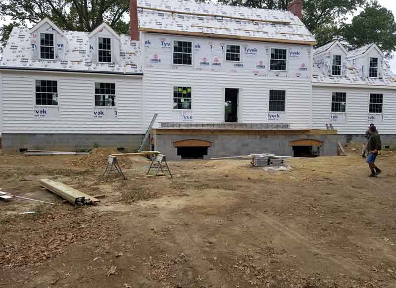 The exterior of a 2 story home shows Tyvek insulation and new siding being installed.