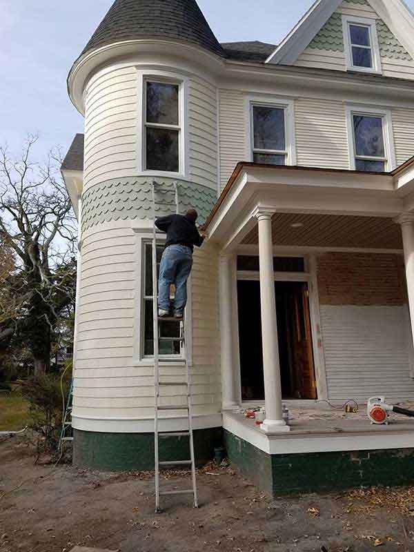 Exterior paint being applied by a person on a ladder.