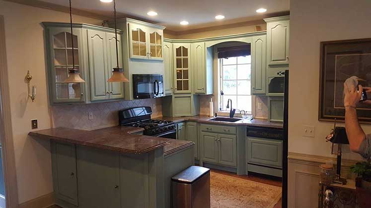 A kitchen painted a medium shade of green and brown granite countertops has fresh tile.