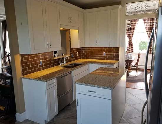 A brick backsplash has a beige granite counter and white cabinetry.